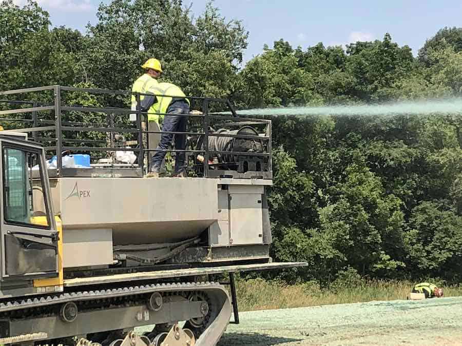 how to choose a hydroseeder - two workers stand on the deck of an Apex hydroseeder as they spray hydroseed over the ground