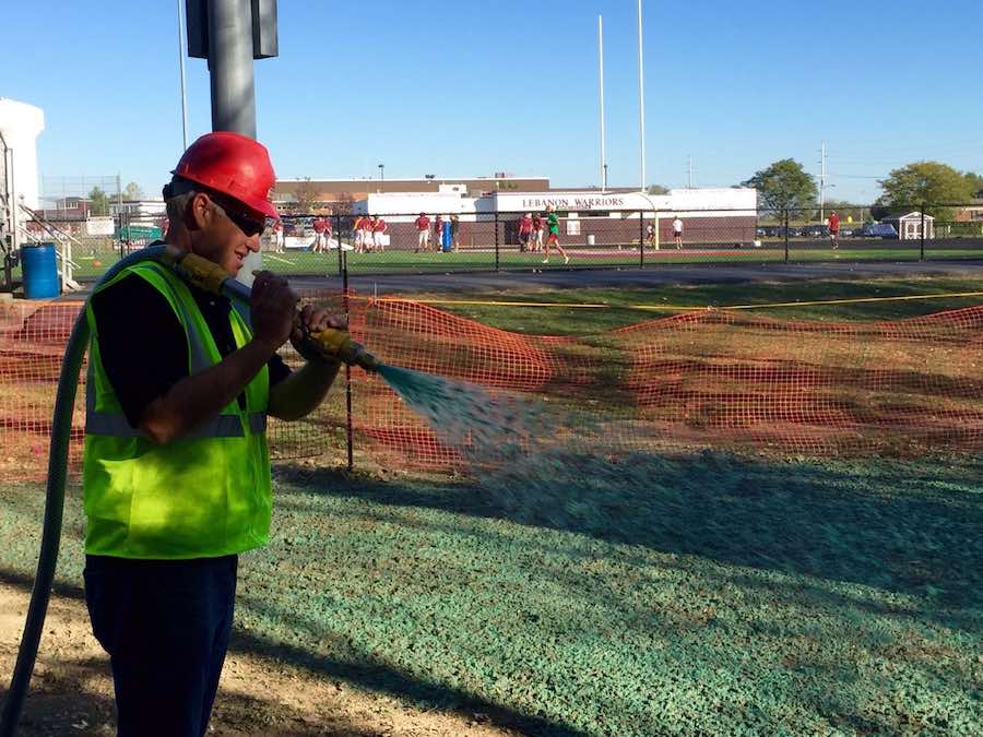 Hydroseeding for athletic fields - a work holds a hose over their shoulder and sprays hydroseed over a sports field