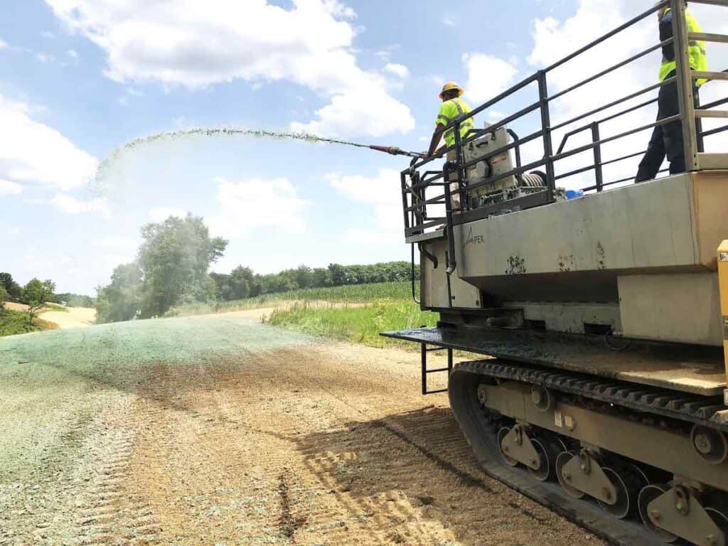 common hydroseeding mistakes to avoid. A worker stands on top of a large hydroseeder, spraying hydroseed overe a bare portion of land.